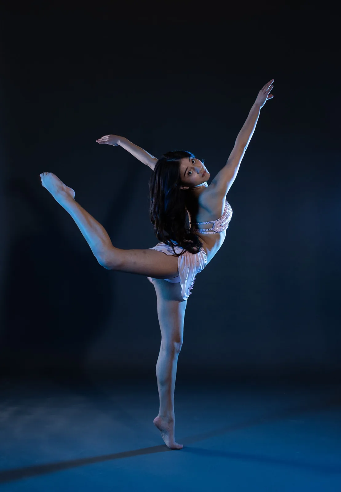 Dancer under blue studio lighting holding a high back extension