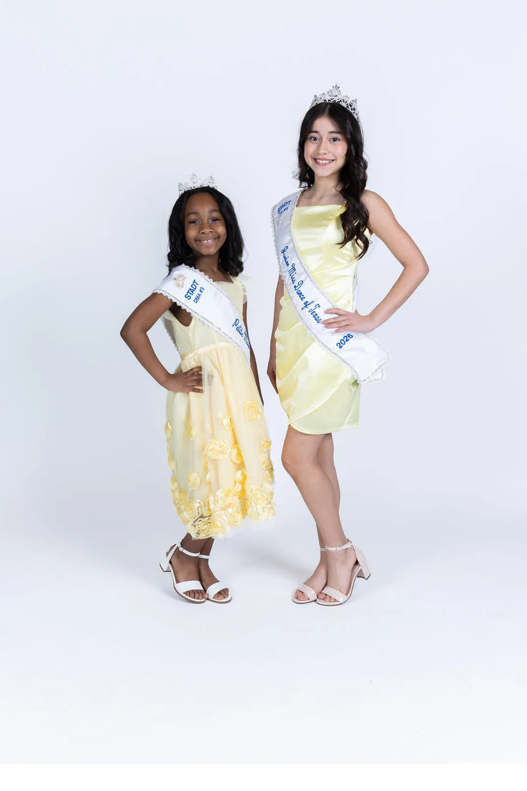 Two young dancers in yellow dresses wearing crowns and sashes