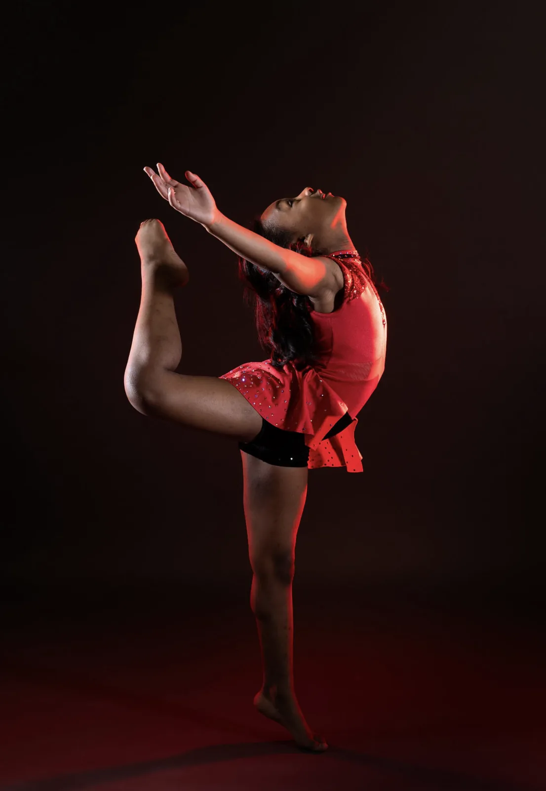 Young dancer in a red costume performing under dramatic red lighting