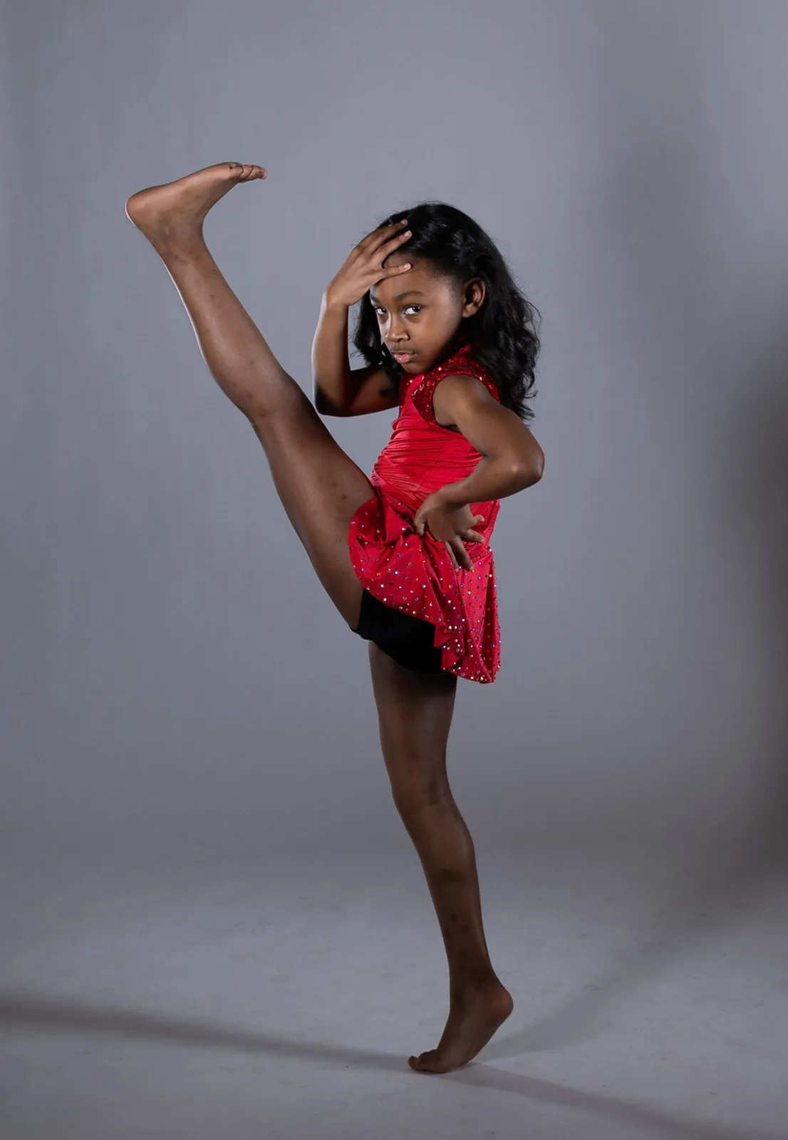 Young dancer in a red costume performing a high leg extension
