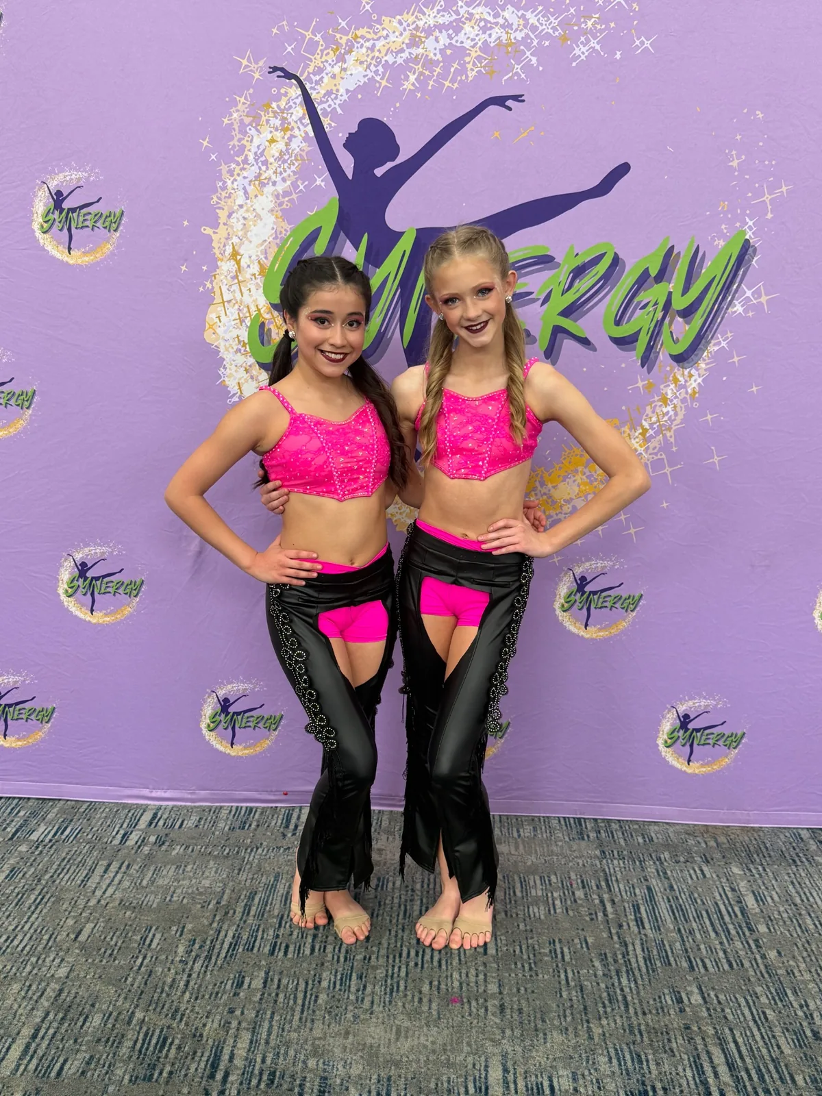 Two young dancers in bright pink and black competition costumes